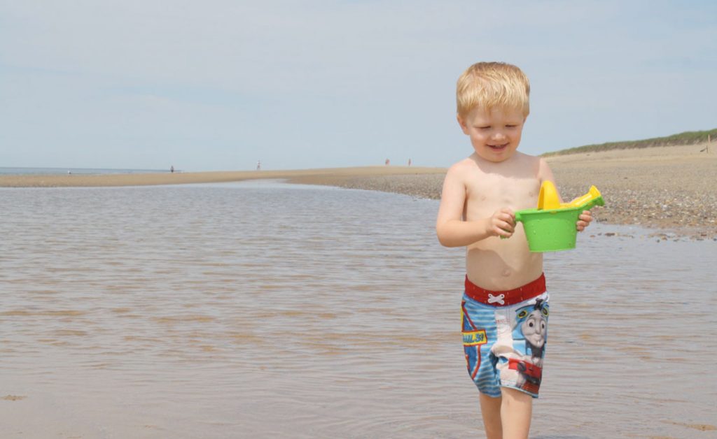 A boy playing with a watering can in a sandbar pool.